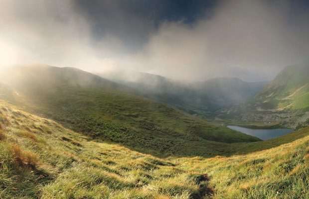 Cloud breaking over a high green cirque above a mountain tarn